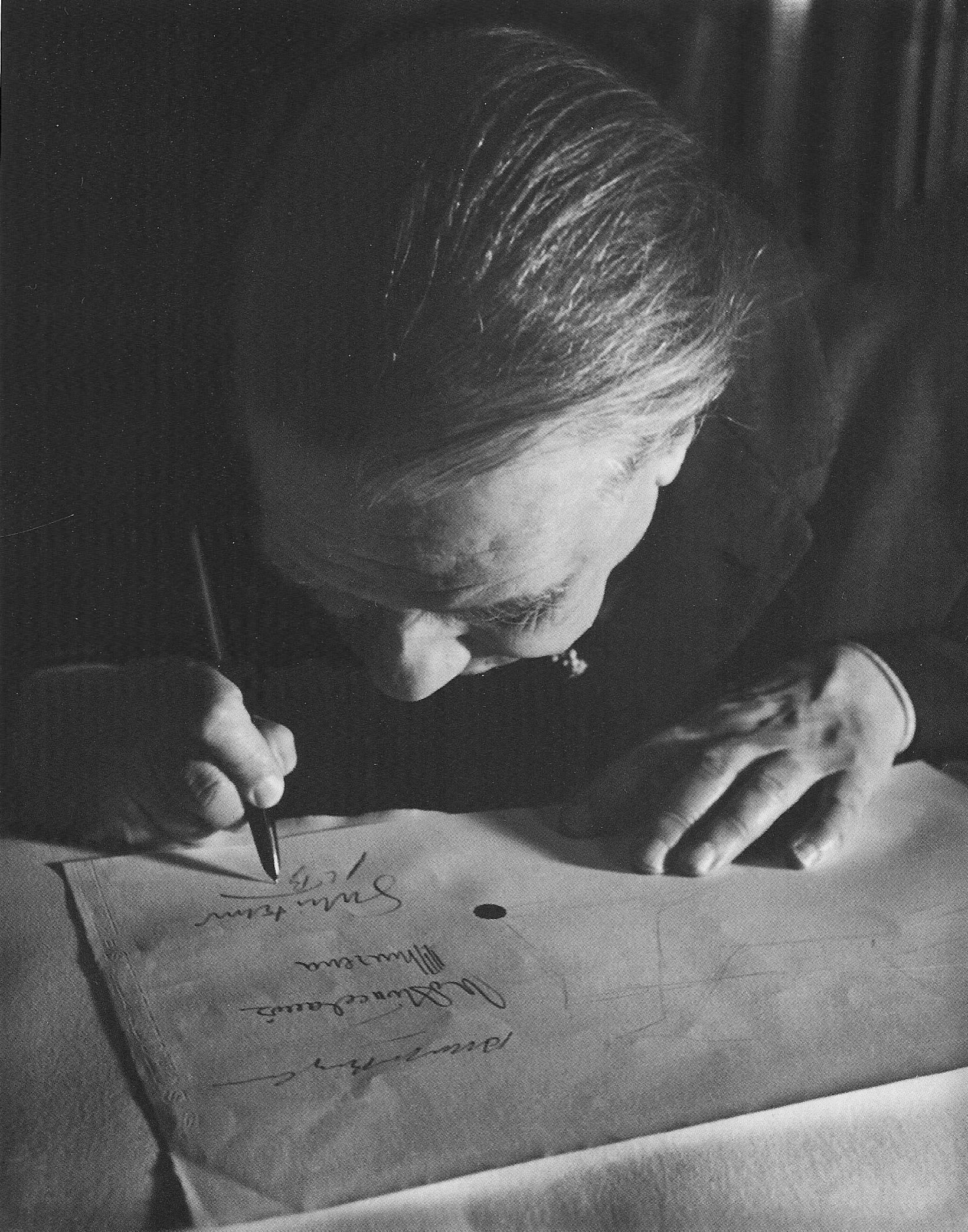 Jorge Luis Borges signing his name, his face is close to the paper 