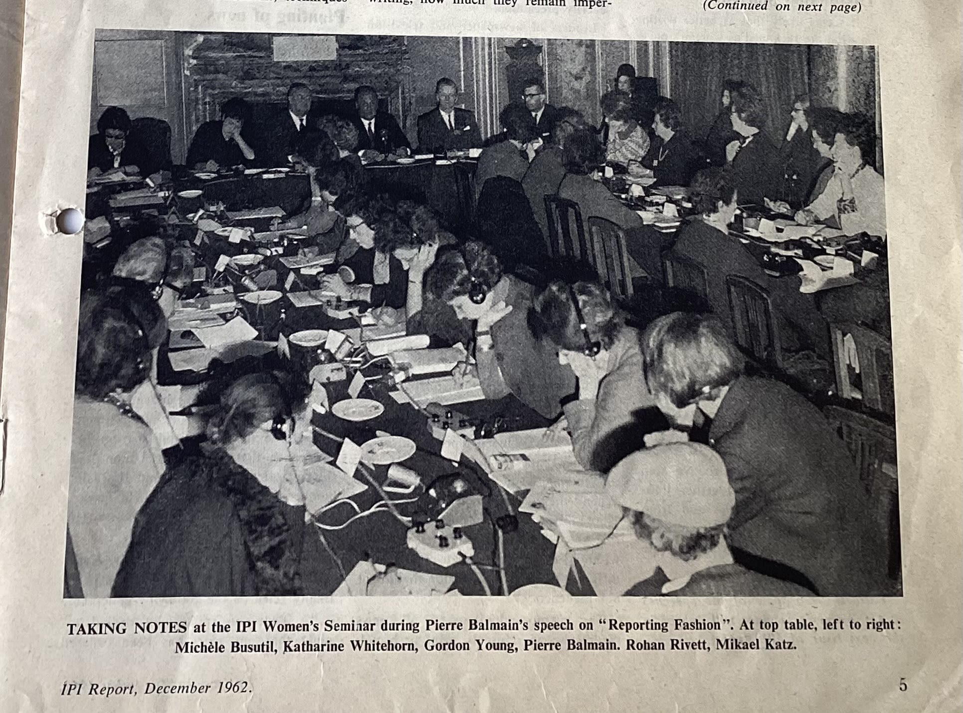 photo of women seated and taking notes, some are wearing headphones and listening to an interpreter
