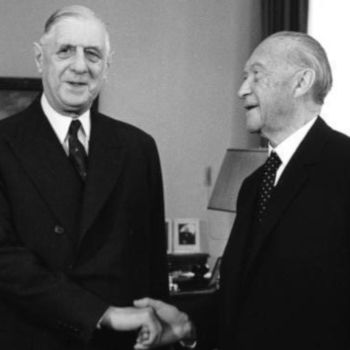 French President Charles de Gaulle (left) shaking hands with German chancellor Konrad Adenauer (right). Both men are smiling. 